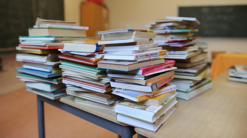 Bücher stapeln sich auf einem Tisch in einem Klassenzimmer.