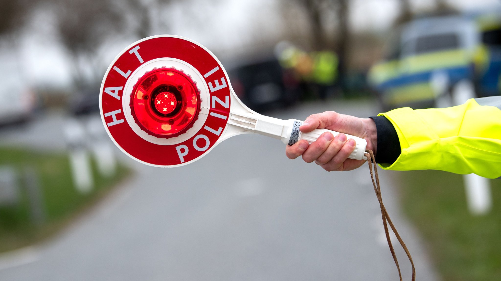 Ein Beamter hält eine Polizeikelle mit der Aufschrift "Halt Polizei" in die Luft.