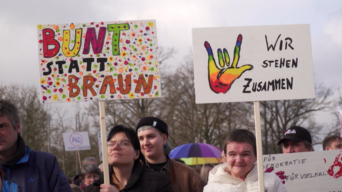 Menschen tragen Plakate mit der Aufschrift: "Bunt statt Braun", "Für Demokratie und Vielfalt", "AfD" durchgestrichen und "Wir stehen zusammen".