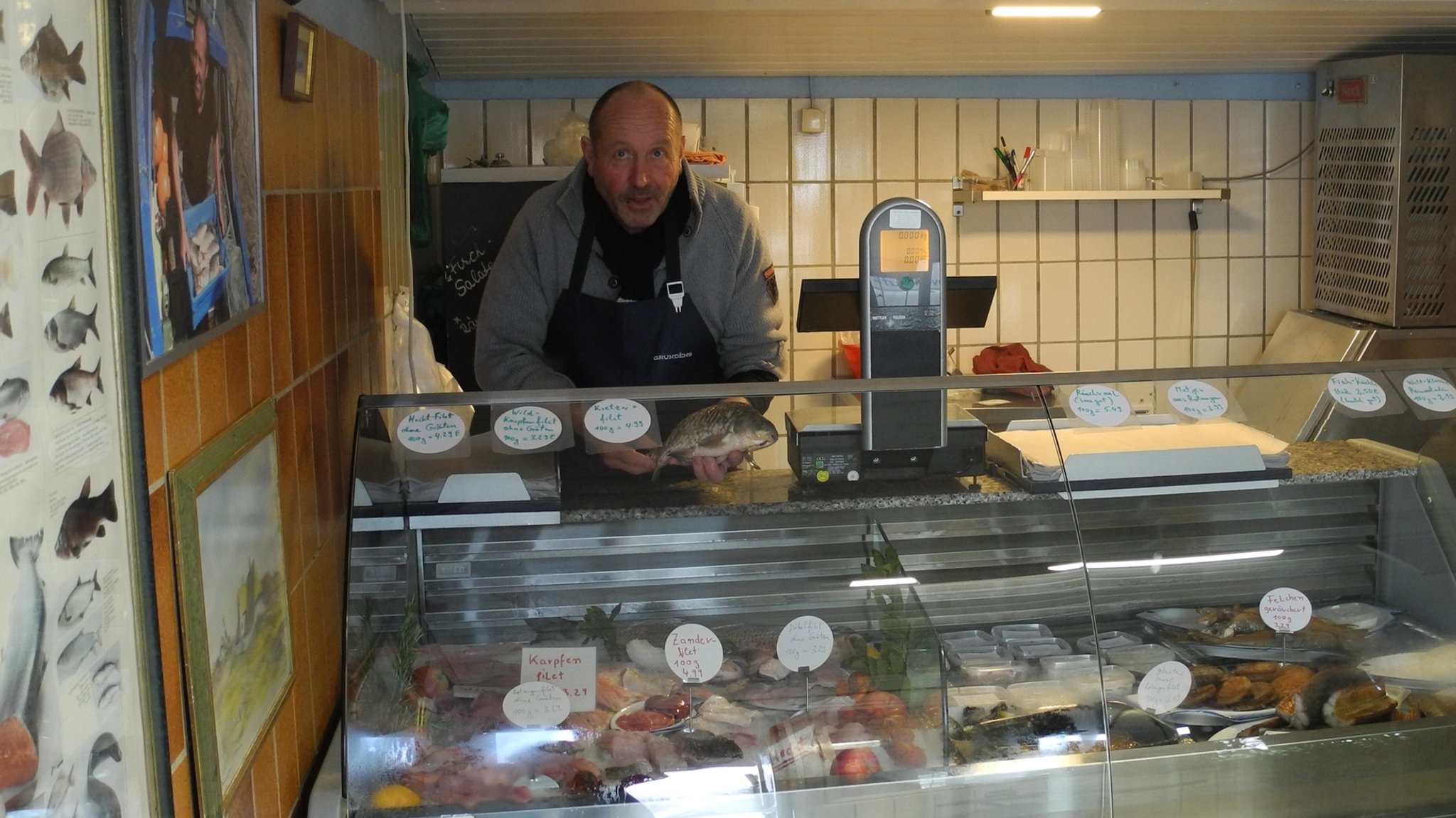 Blick auf eine Fischtheke in einem kleinen Laden. Hinter der Theke steht der Verkäufer mit einem Fisch in der Hand.