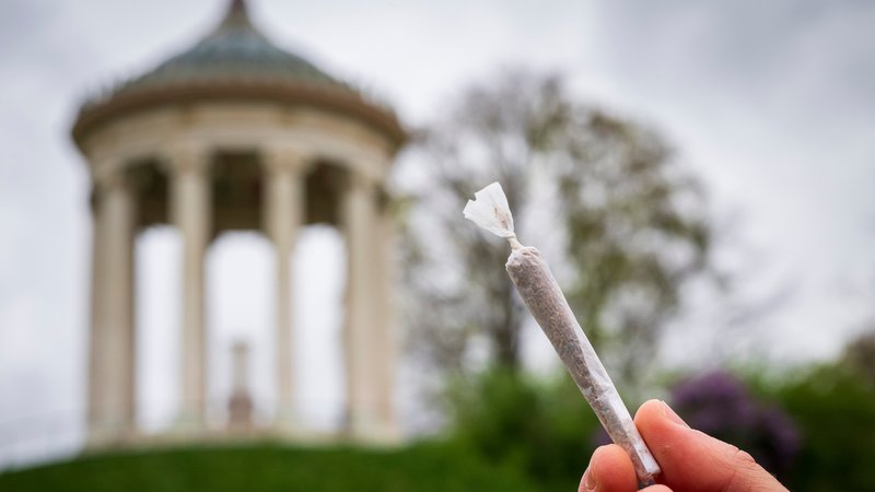 (Archivbild) Ein Mann hält einen Joint vor der Kulisse des Monopteros im Englischen Garten. | Bild: picture alliance/dpa | Peter Kneffel (Archivbild) Ein Mann hält einen Joint vor der Kulisse des Monopteros im Englischen Garten.