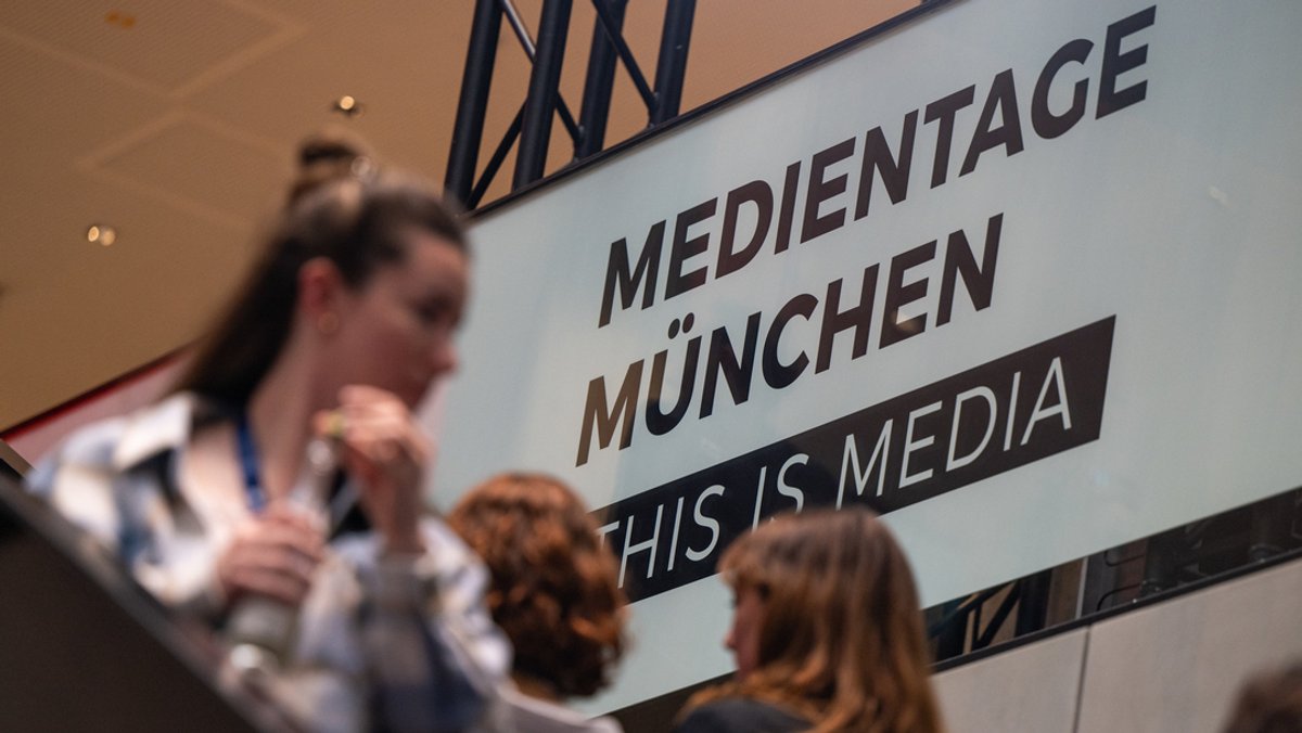 München: Teilnehmer der 37. Medientage München gehen an einer Logowand der Medientage München vorbei. 