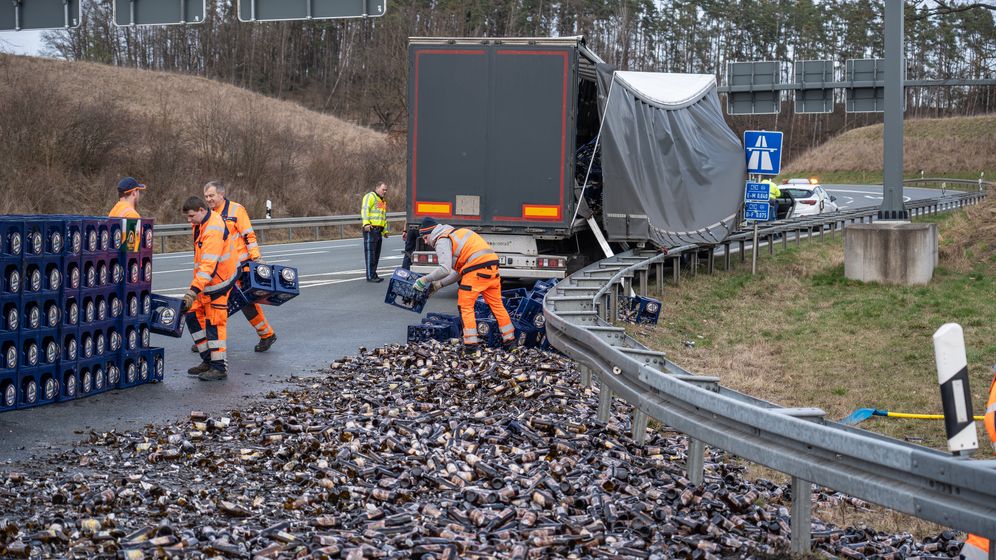 Männer in orangen Anzügen tragen Bierkisten über eine Autobahnauffahrt. Im Hintergrund ein beschädigter Sattelschelpper. | Bild:NEWS5 / Merzbach