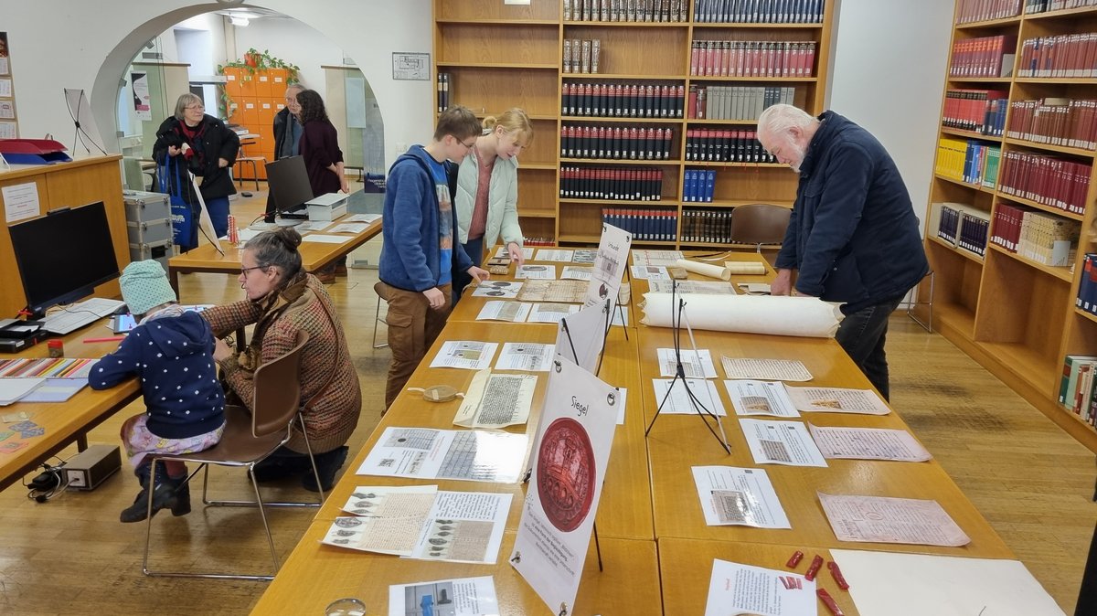 Mehrere Menschen studieren archivarische Schriftstücke. 