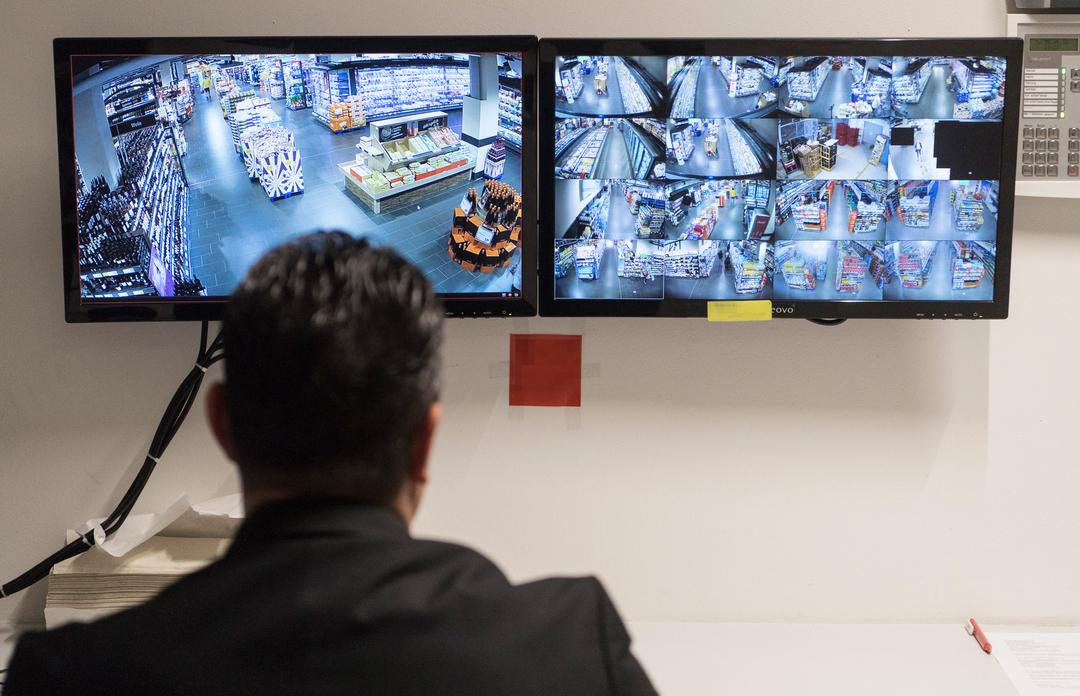 Ein Ladendetektiv sitzt vor Überwachungsmonitoren eines Supermarktes.