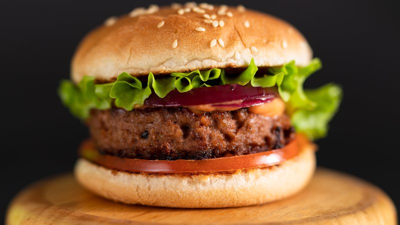 (Symbolbild) Ein Veggie-Burger liegt auf einem Holzteller. | Bild: stock.adobe.com/Yevhenii (Symbolbild) Ein Veggie-Burger liegt auf einem Holzteller.