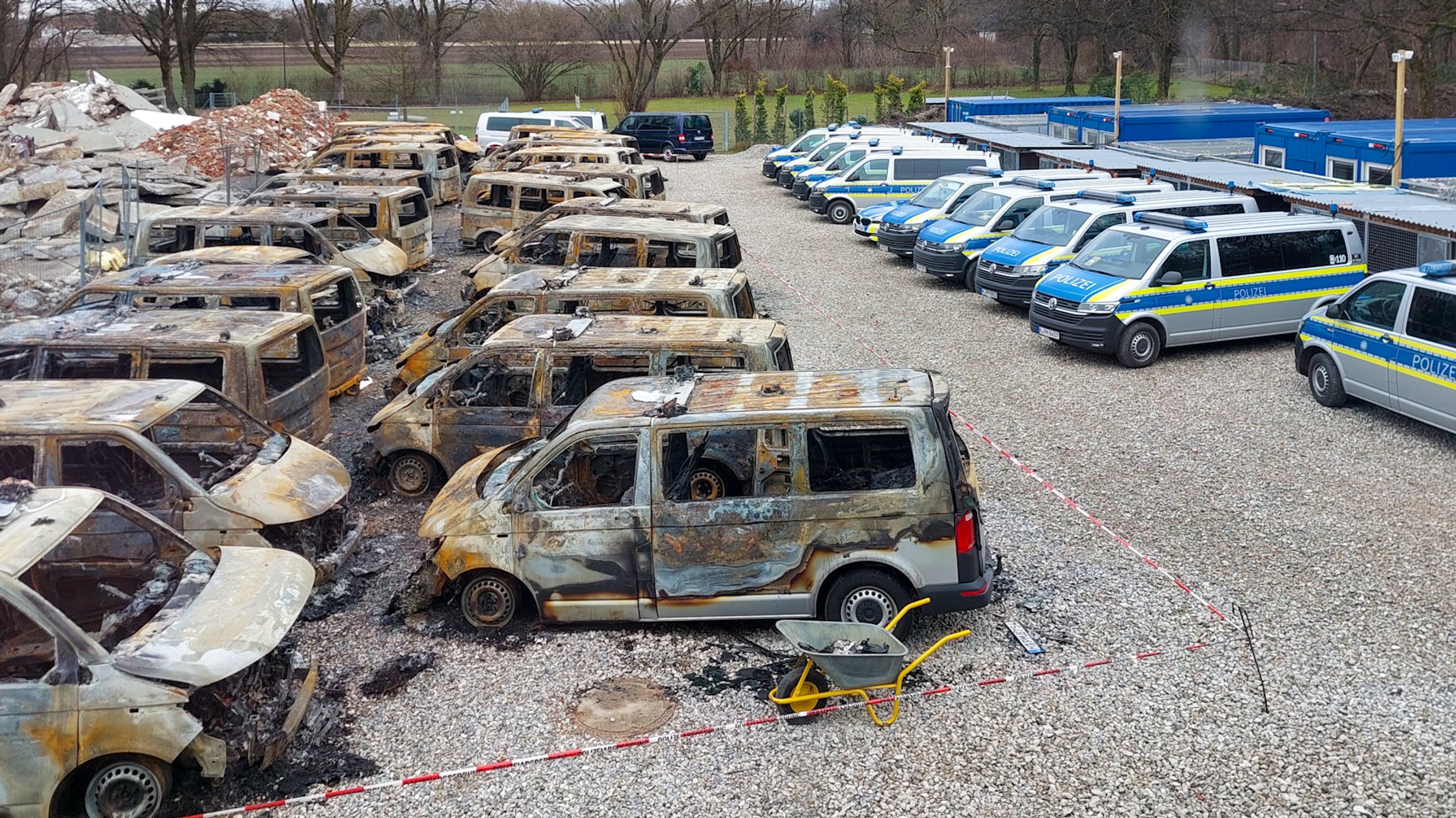 Blick aus der Vogelperspektive auf den Parkplatz der Münchner Polizeihundestaffel. Darauf stehen mehr als 20 völlig ausgebrannte Polizei-Kleinbusse, daneben in einer Reihe etwa zehn intakte Wagen.