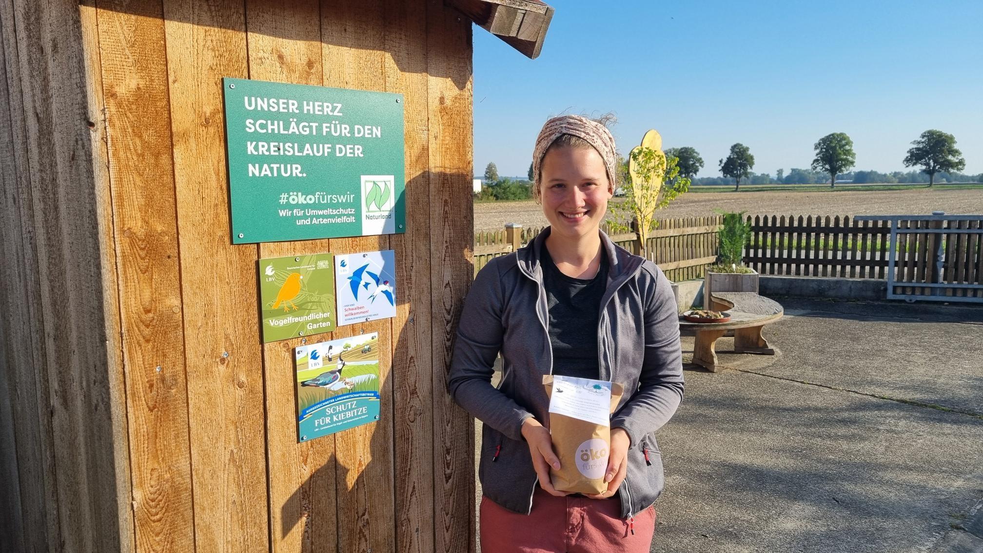 Landwirtin Anna-Maria Bissinger vom "Biohöfle" steht neben einer Holzhütte mit einer Packung "Höflemehl mit Kiebitz-Schutz"