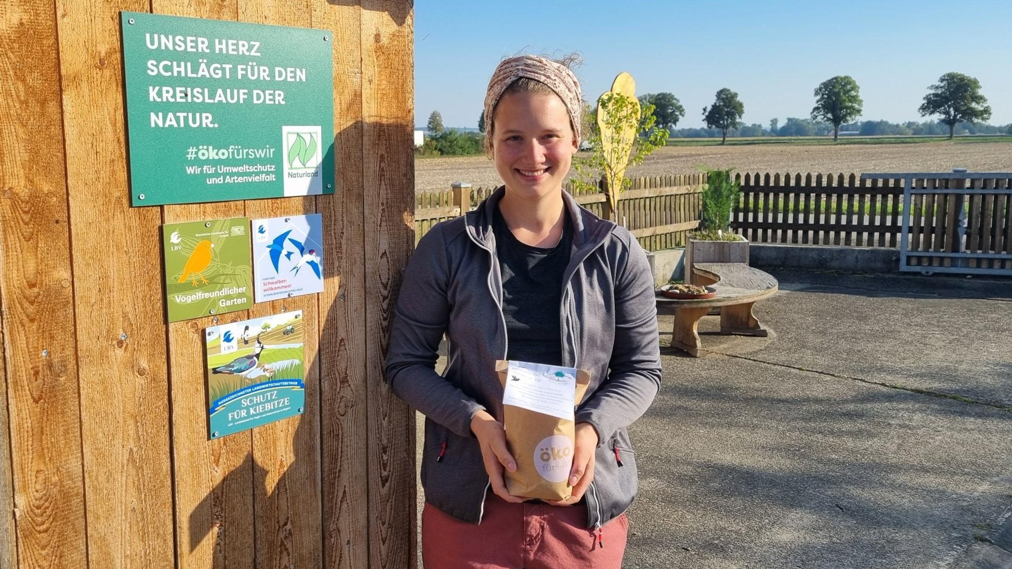 Landwirtin Anna-Maria Bissinger vom "Biohöfle" steht neben einer Holzhütte mit einer Packung "Höflemehl mit Kiebitz-Schutz"