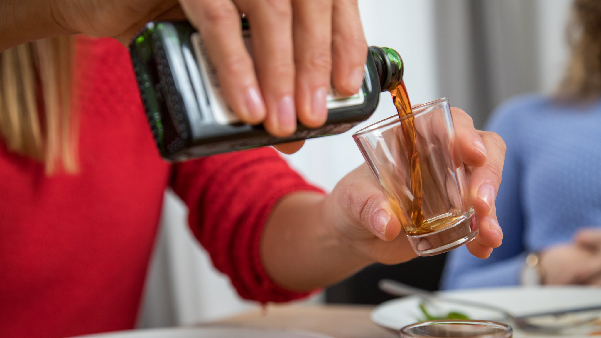 Nahaufnahme von Händen: Frau gießt einen Schnaps in ein Glas ein