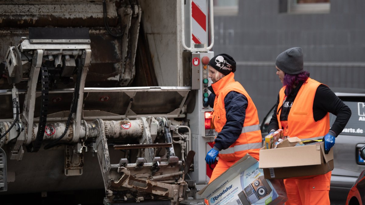 Zwei Abfallwerkerinnen werfen Pappkisten in ein Müllfahrzeug (Symbolbild)