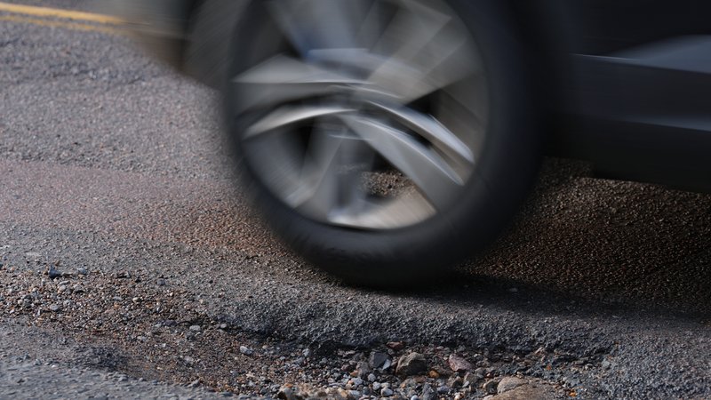 Ein Auto fährt auf einer Straße. Ein Schlagloch ist am Boden zu sehen. | Bild: picture alliance / empics | Yui Mok Ein Auto fährt auf einer Straße. Ein Schlagloch ist am Boden zu sehen.
