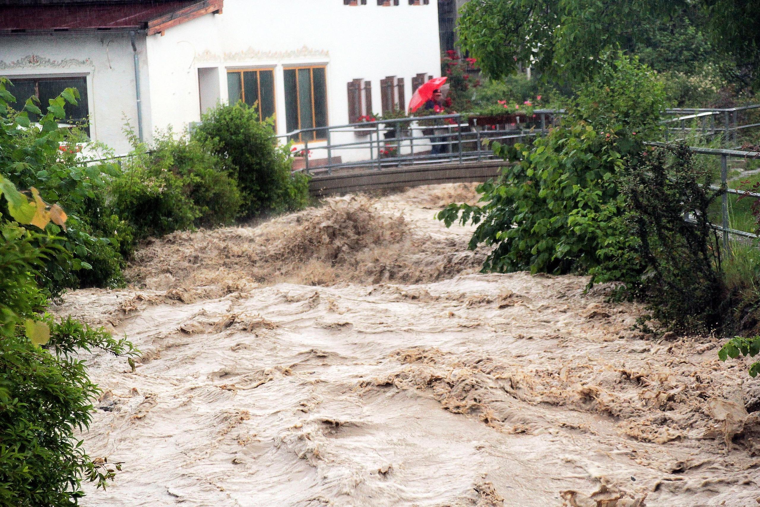 03.06.2024, Bayern, Bad Feilnbach: Ein Passant steht auf einer Brücke über den Auerbach im Ortsteil Au im Landkreis Rosenheim. Der Bach entwickelte sich am Montag nach Starkregen zu einer reißenden Flut. Foto: Josef Reisner/dpa +++ dpa-Bildfunk +++
