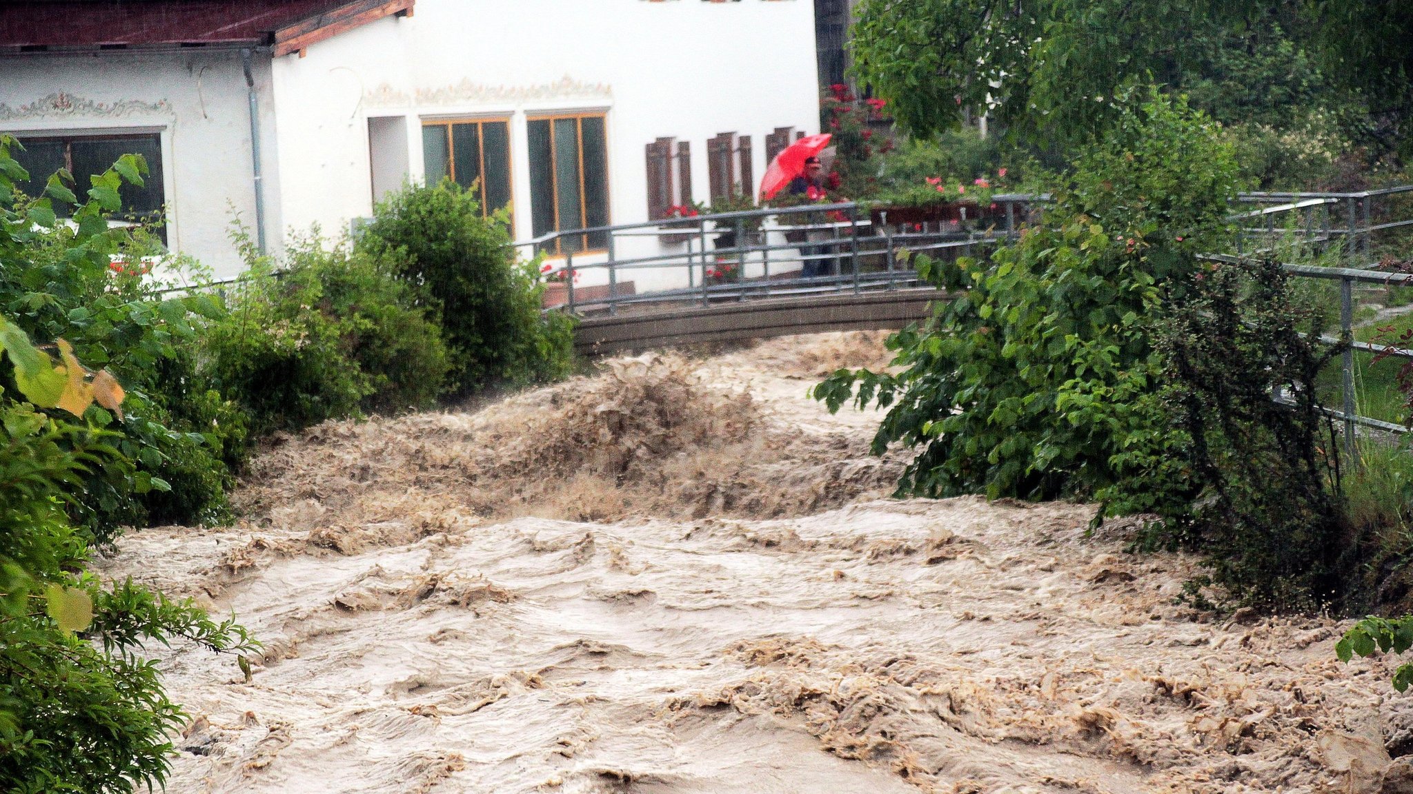 03.06.2024, Bayern, Bad Feilnbach: Ein Passant steht auf einer Brücke über den Auerbach im Ortsteil Au im Landkreis Rosenheim. Der Bach entwickelte sich am Montag nach Starkregen zu einer reißenden Flut. Foto: Josef Reisner/dpa +++ dpa-Bildfunk +++