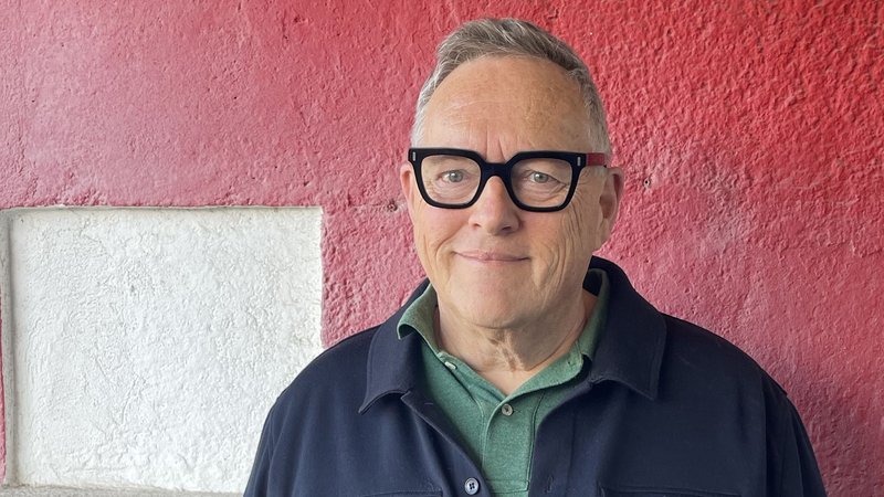 Autor Thomas Meinecke steht lächelnd und mit großer schwarzer Brille vor einer roten Wand | Bild: Michaela Melián / Suhrkamp Verlag Autor Thomas Meinecke steht lächelnd und mit großer schwarzer Brille vor einer roten Wand