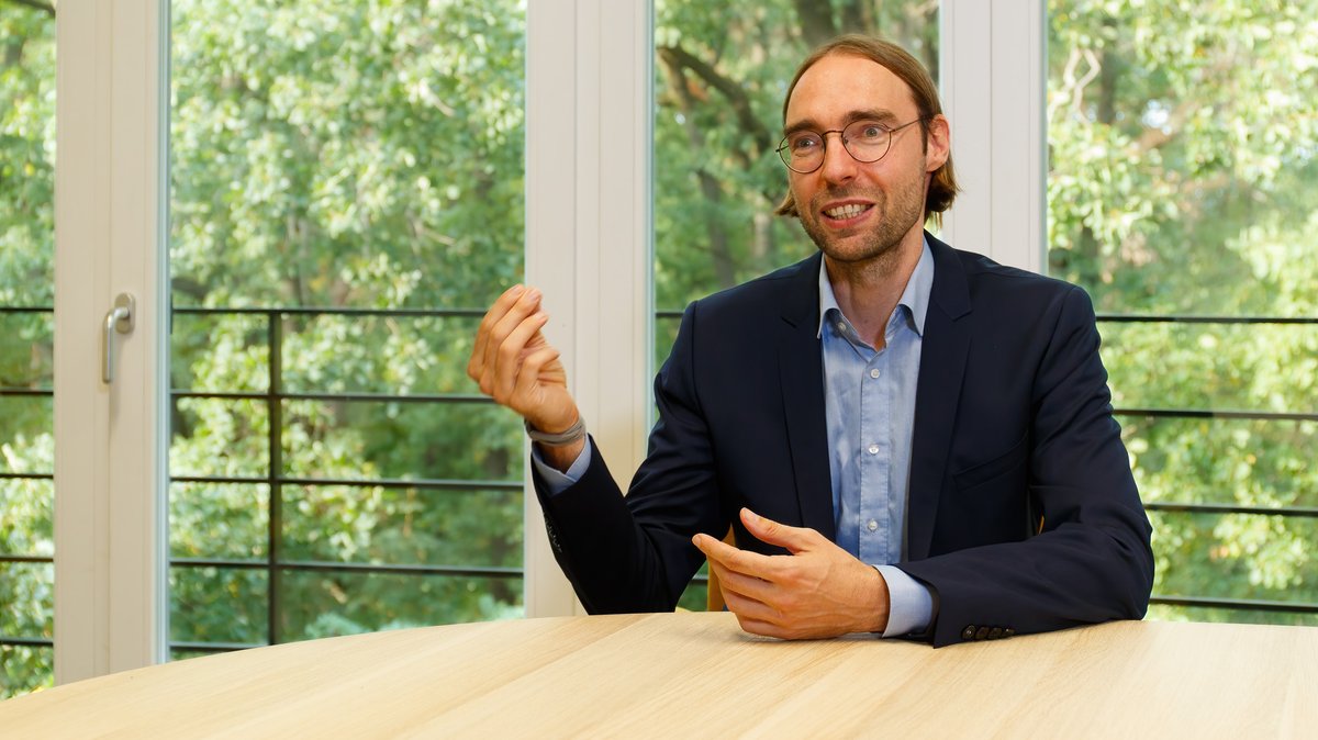 Ein Mann mit Brille sitzt gestikulierend am Tisch, es ist Falko Ueckerdt, Energieforscher am Potsdam-Institut für Klimafolgenforschung