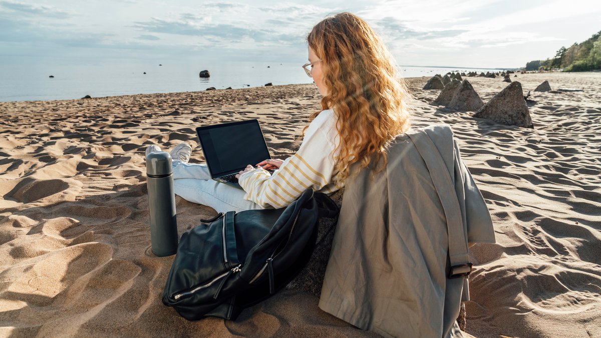 Symbolbild: Eine Frau mit Laptop und Thermoskanne am Strand