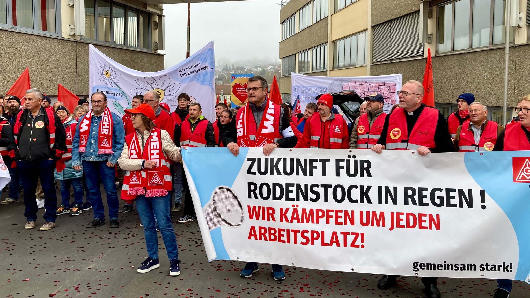 Beschäftigte von Rodenstock stehen mit Schals und Plakaten vor ihrem Unternehmen.