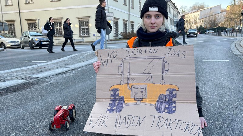 Eine Klimaaktivistin der "Letzten Generation" mit einem Schild: "Wir dürfen das, wir haben Traktoren". 