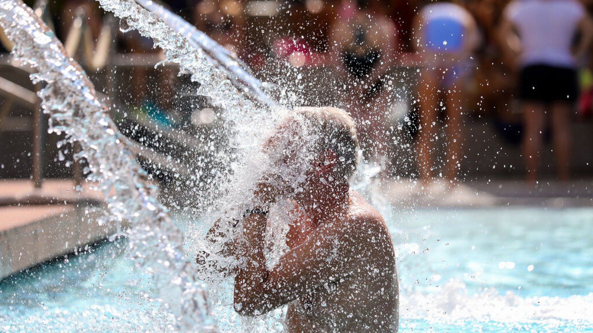 19.07.2023, Baden-Württemberg, Sigmaringen: Ein Mann erfrischt sich im Donaubad unter einer Wasserfontäne. Bis zum Wochenende bleibt das Wetter in Baden-Württemberg sommerlich-freundlich mit Temperaturen bis zu 29 Grad - doch auch Schauer werden erwartet. Foto: Thomas Warnack/dpa +++ dpa-Bildfunk +++