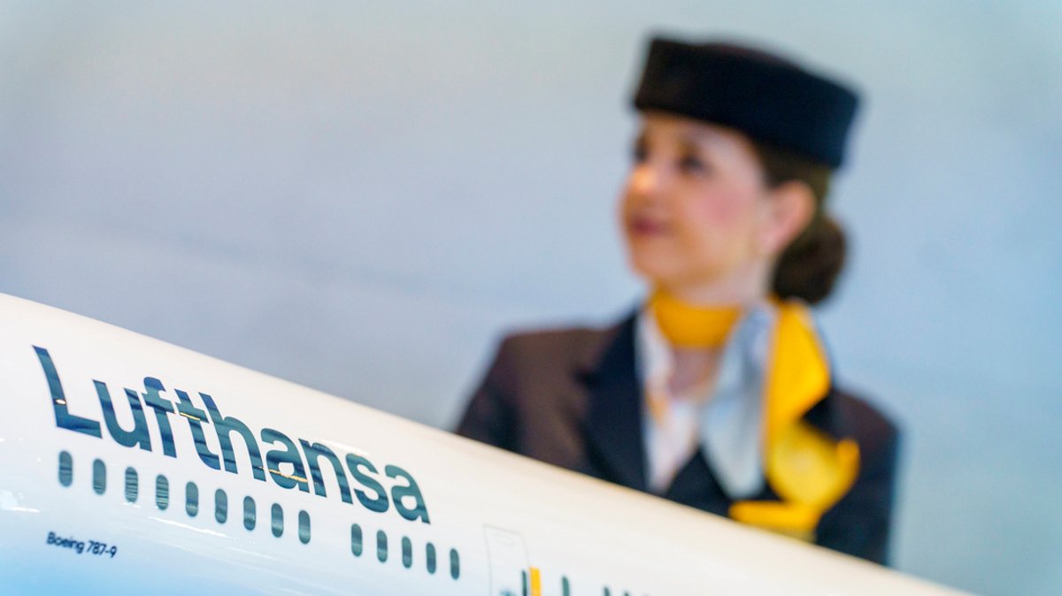 Eine Flugbegleiterin steht hinter einem Modell einer Lufthansamaschine. 
