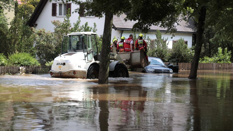 Rettungskräfte sitzen auf der Schaufel eines Radladers, der rund 30 sm im Hochwasser auf einer Straße steht, | Bild: BR I Axel Mölkner-Kappl Rettungskräfte sitzen auf der Schaufel eines Radladers, der rund 30 sm im Hochwasser auf einer Straße steht,
