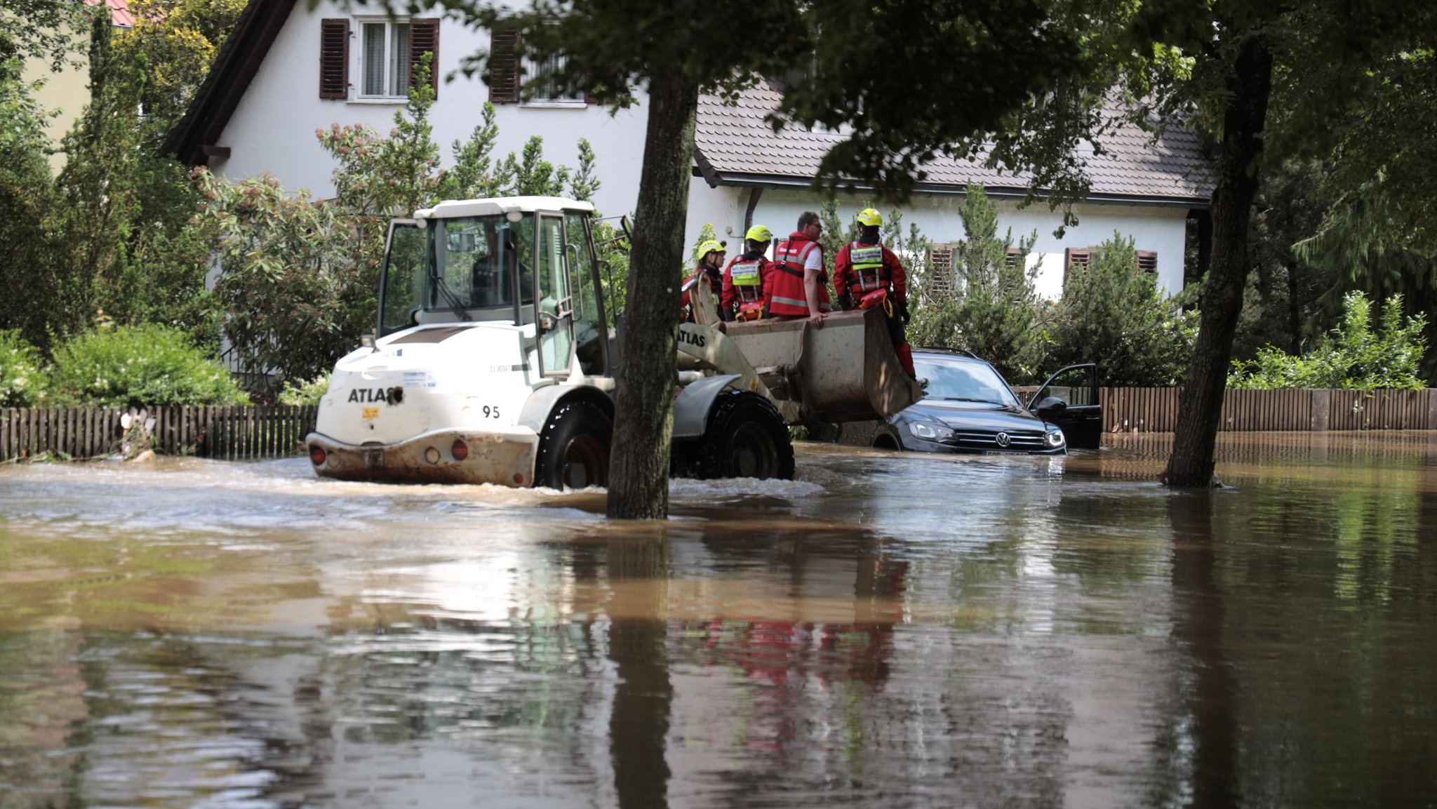 Rettungskräfte sitzen auf der Schaufel eines Radladers, der rund 30 sm im Hochwasser auf einer Straße steht,