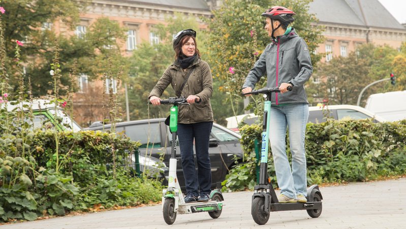 Zwei Erwachsene mit Helm auf E-Scootern | Bild: picture alliance Zwei Erwachsene mit Helm auf E-Scootern