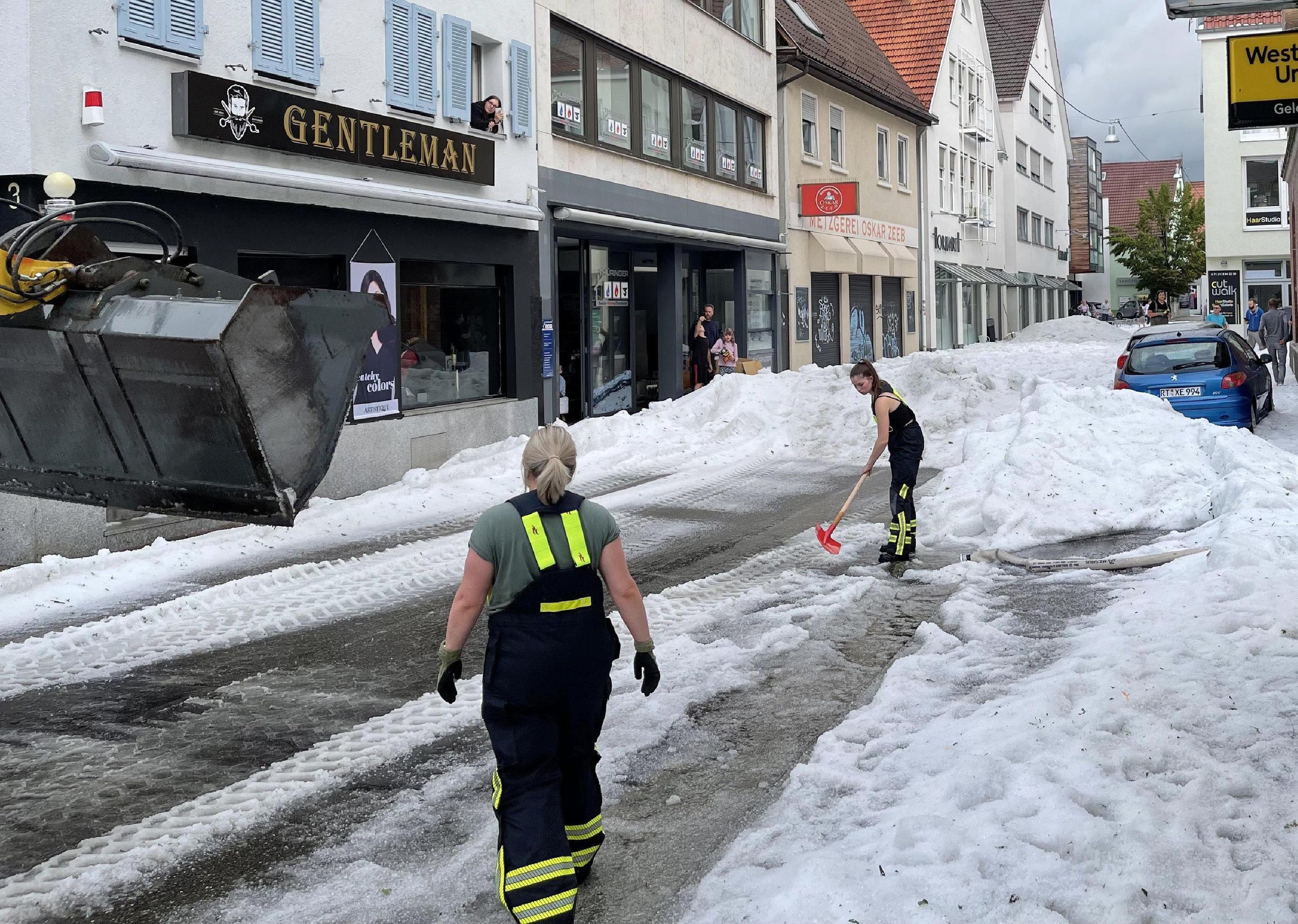 Einsatzkräfte der Feuerwehr räumen in Reutlingen im August 2023 Hagel von einer Straße.