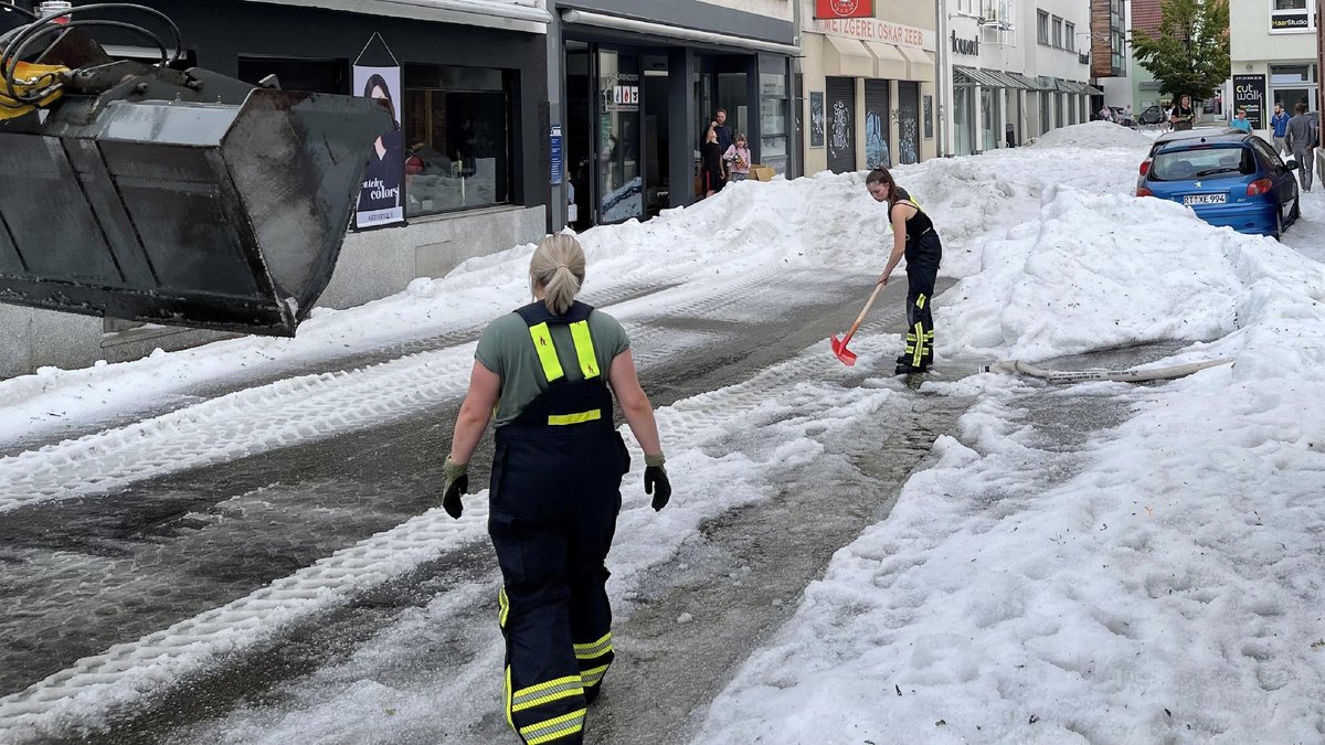 Einsatzkräfte der Feuerwehr räumen in Reutlingen im August 2023 Hagel von einer Straße.