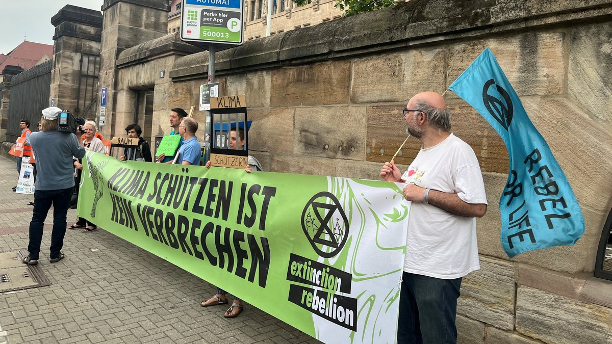 Menschen mit Transparent "Klimaschutz ist kein Verbrechen" vor der Mauer des Justizpalastes in Nürnberg.