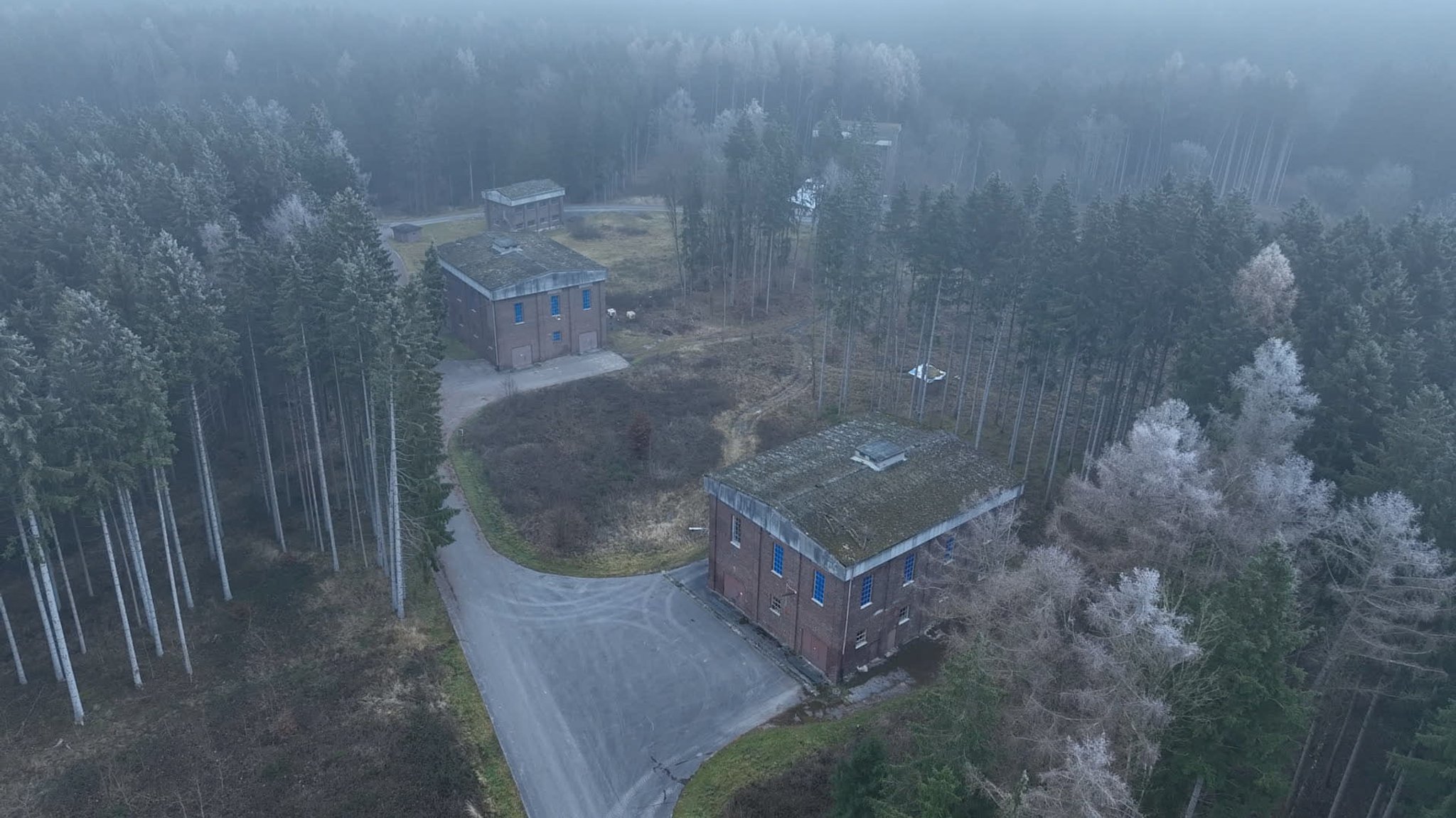 Drohnenaufnahme dreier Backsteingebäude. Umgeben von Wald.