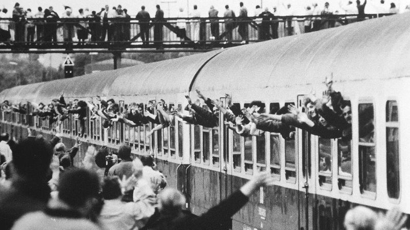 Ein Zug fährt in den Hofer Bahnhof und viele Menschen jubeln ihm zu.