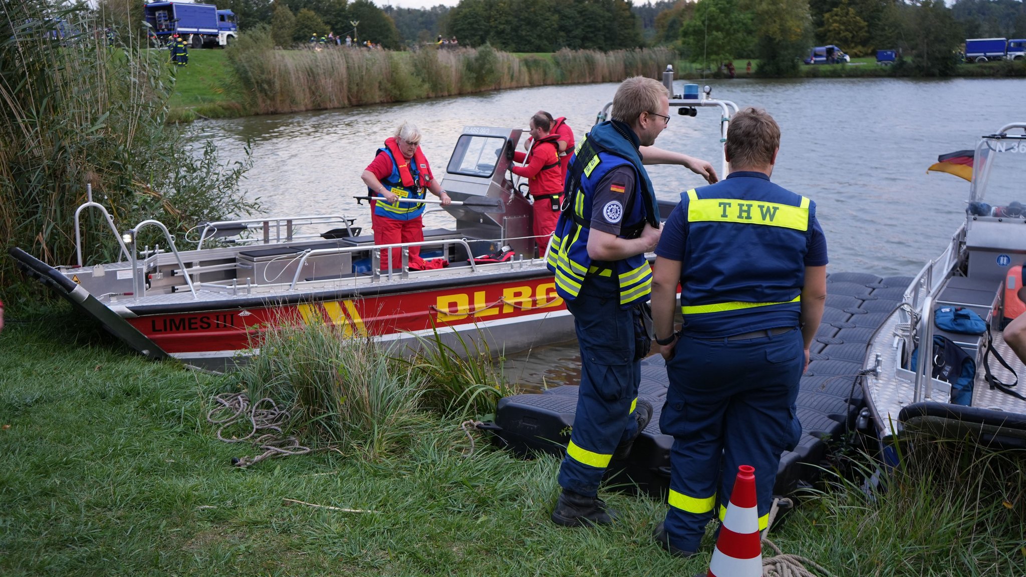 Einsatzkräfte von THW und DLRG mit Boot am Ufer eines Sees.