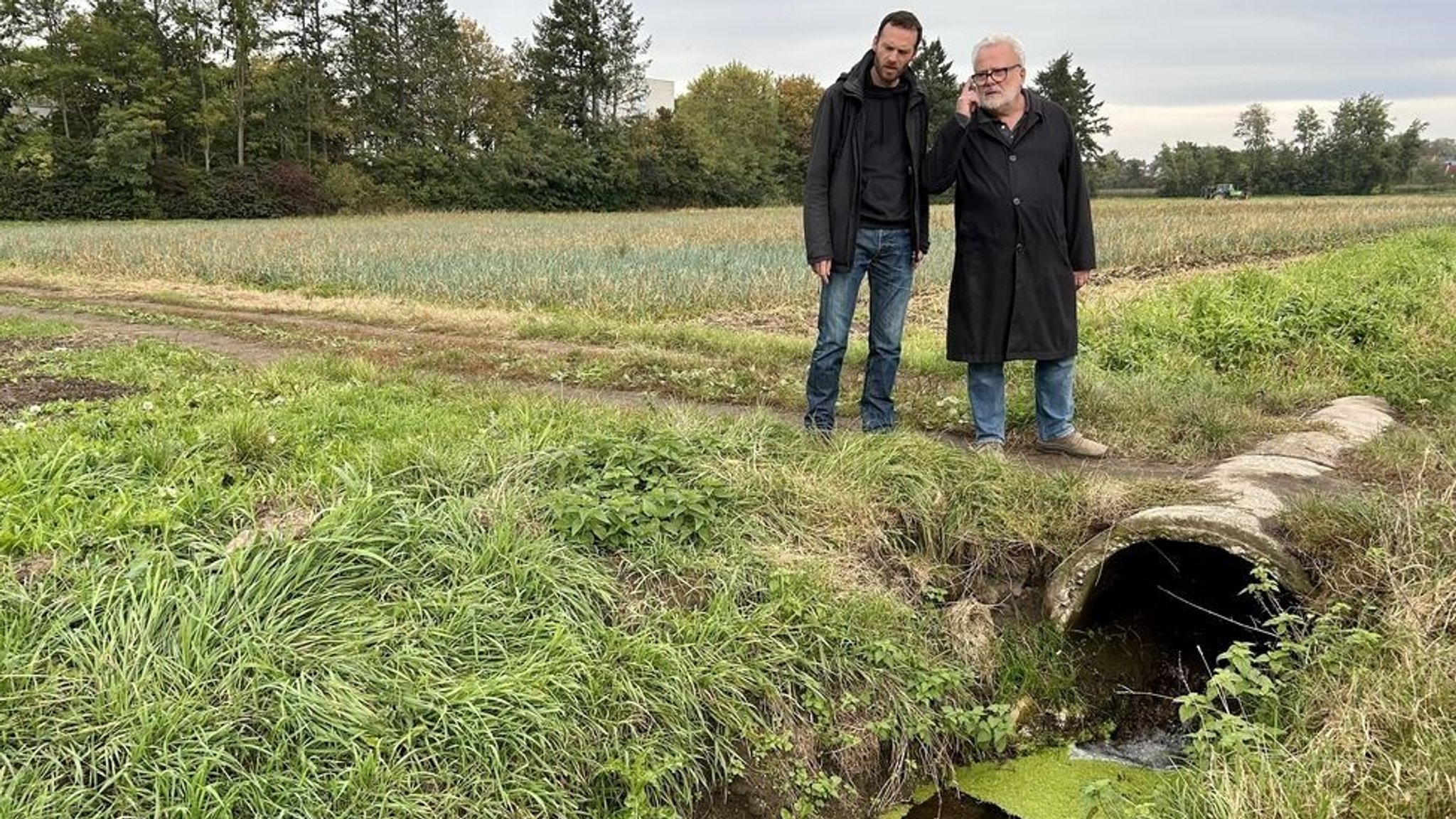 Zwei Männer stehen auf einem Acker an einem Bewässerungsgraben.