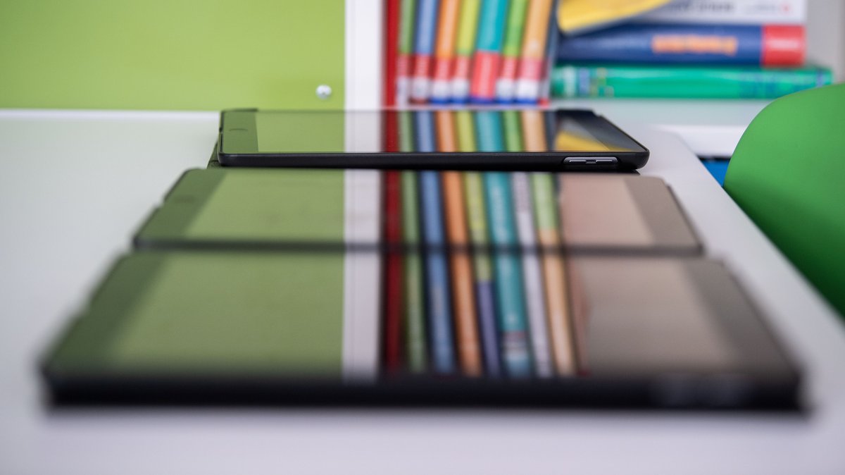 Drei Tablets liegen nebeneinander in einem Klassenzimmer auf einem Tisch (Symbolbild)