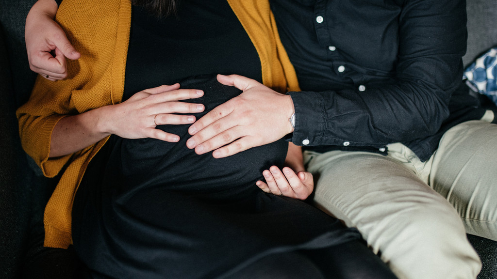 Eine schwangere Frau und ihr Partner sitzen zusammen auf dem Sofa.