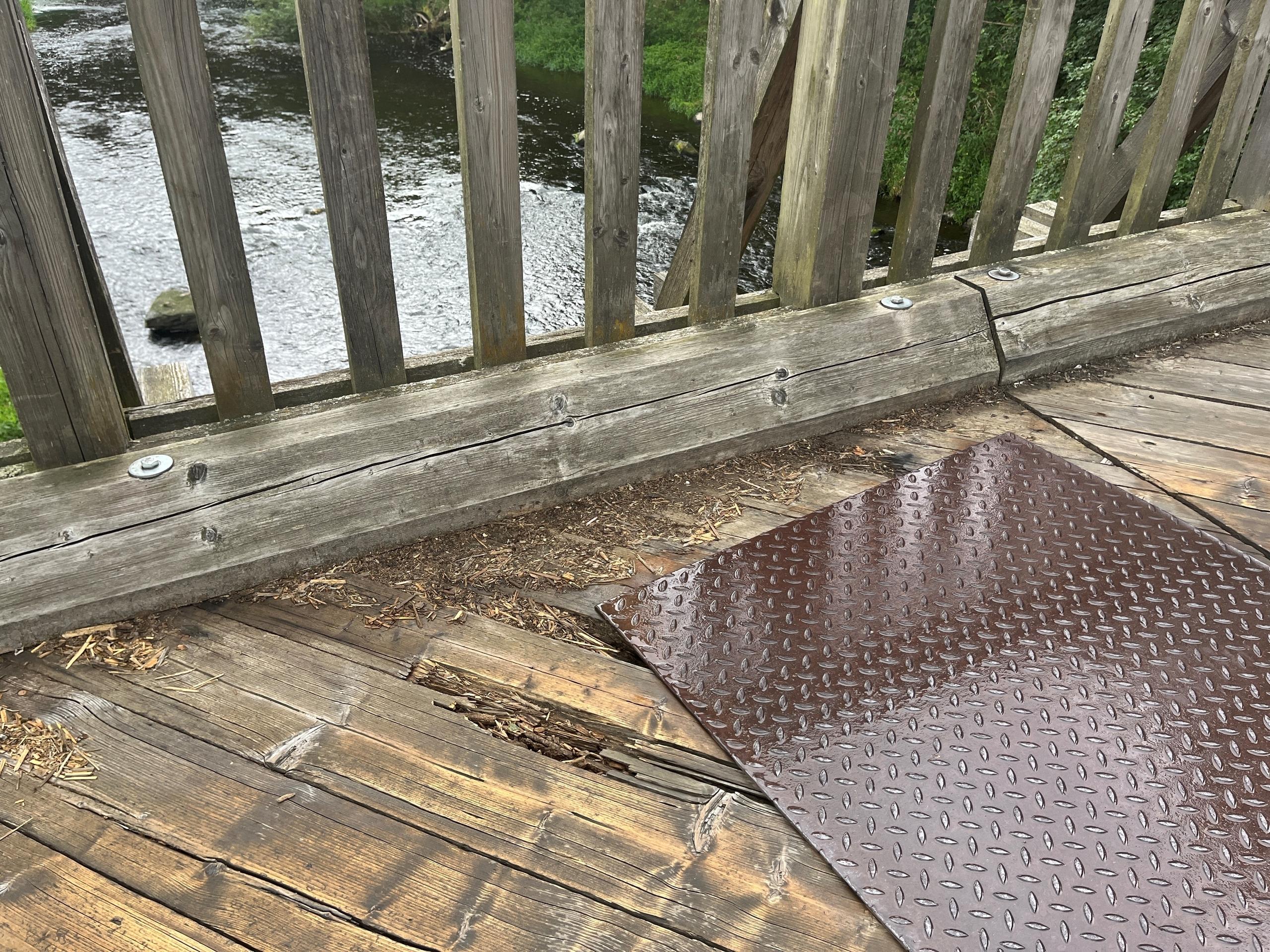 Über den Holzbohlen einer maroden Brücke liegt eine Metallplatte