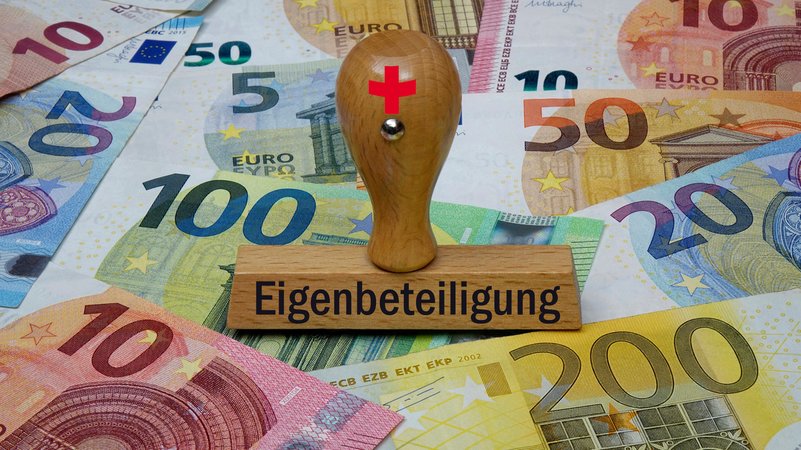 (Symbolbild) Stempel mit der Aufschrift Eigenbeteiligung. Im Hintergrund liegen Geldscheine. | Bild: picture alliance / Sascha Steinach (Symbolbild) Stempel mit der Aufschrift Eigenbeteiligung. Im Hintergrund liegen Geldscheine.
