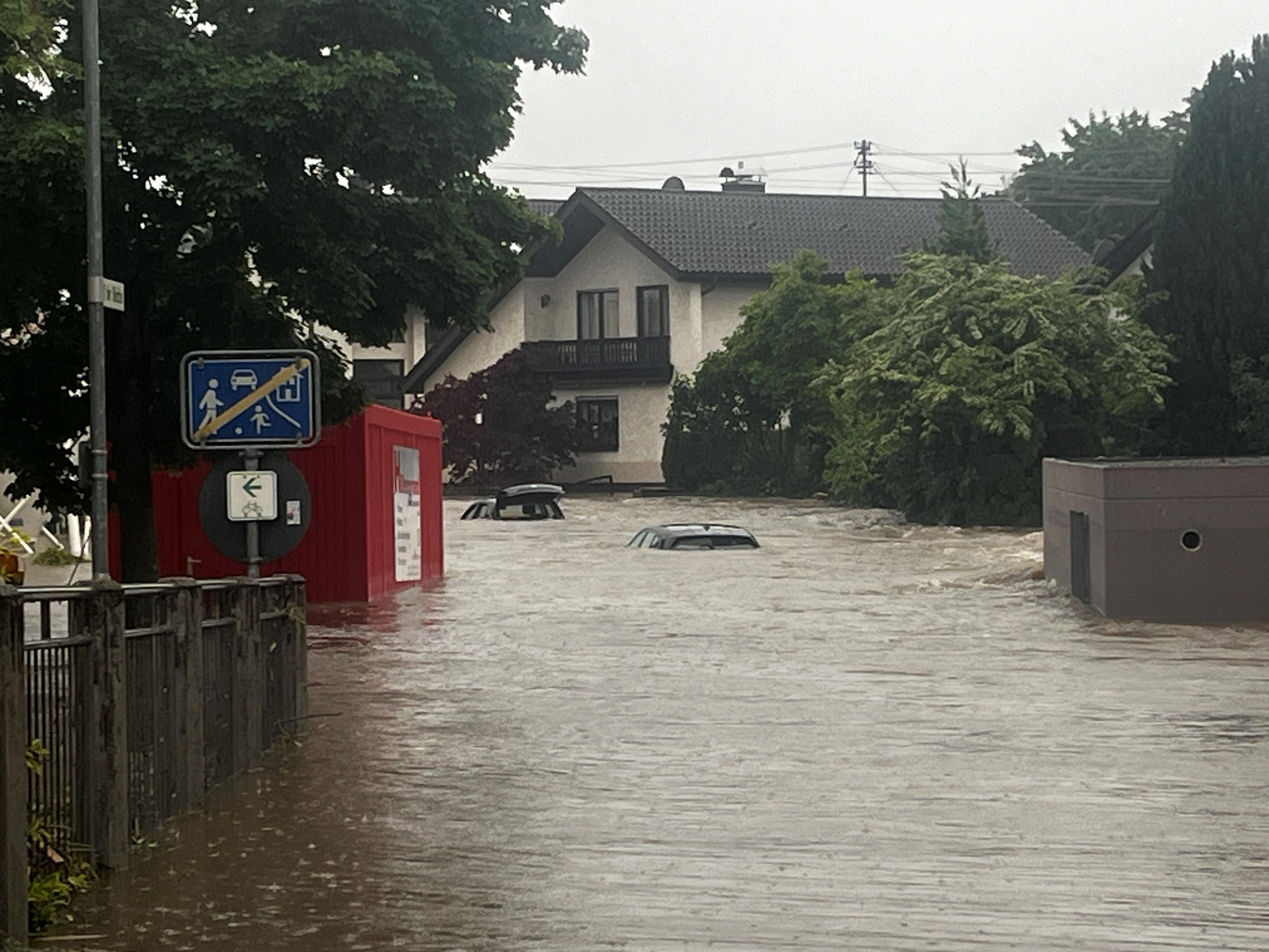 Eine überflutete Straße in einem Wohngebiet, aus dem Wasser ragen zwei Autos.