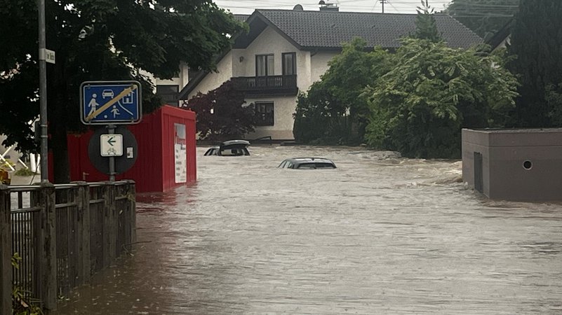 Eine überflutete Straße in einem Wohngebit, aus dem Wasser ragen zwei Autos.
