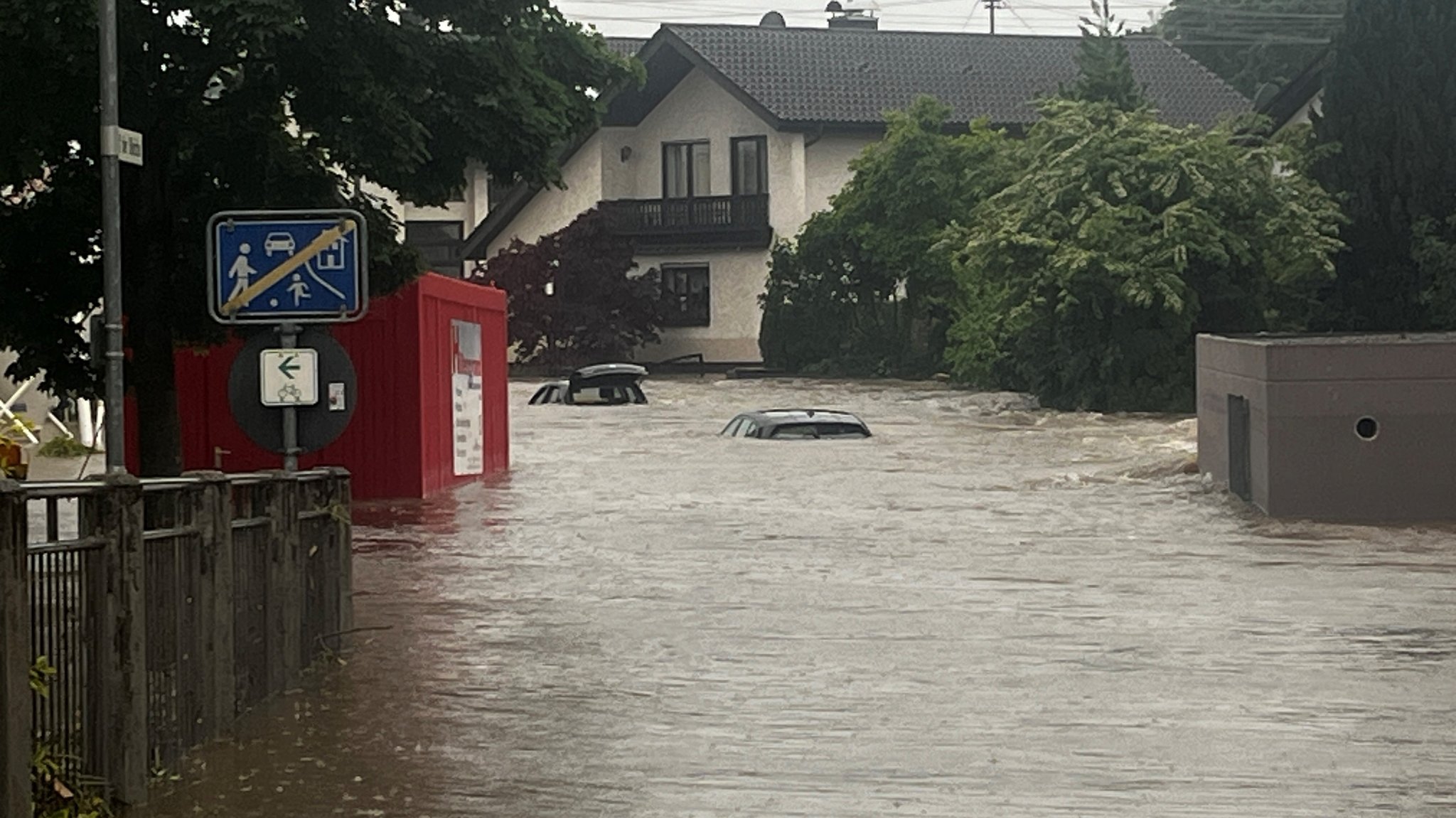 Eine überflutete Straße in einem Wohngebiet, aus dem Wasser ragen zwei Autos.