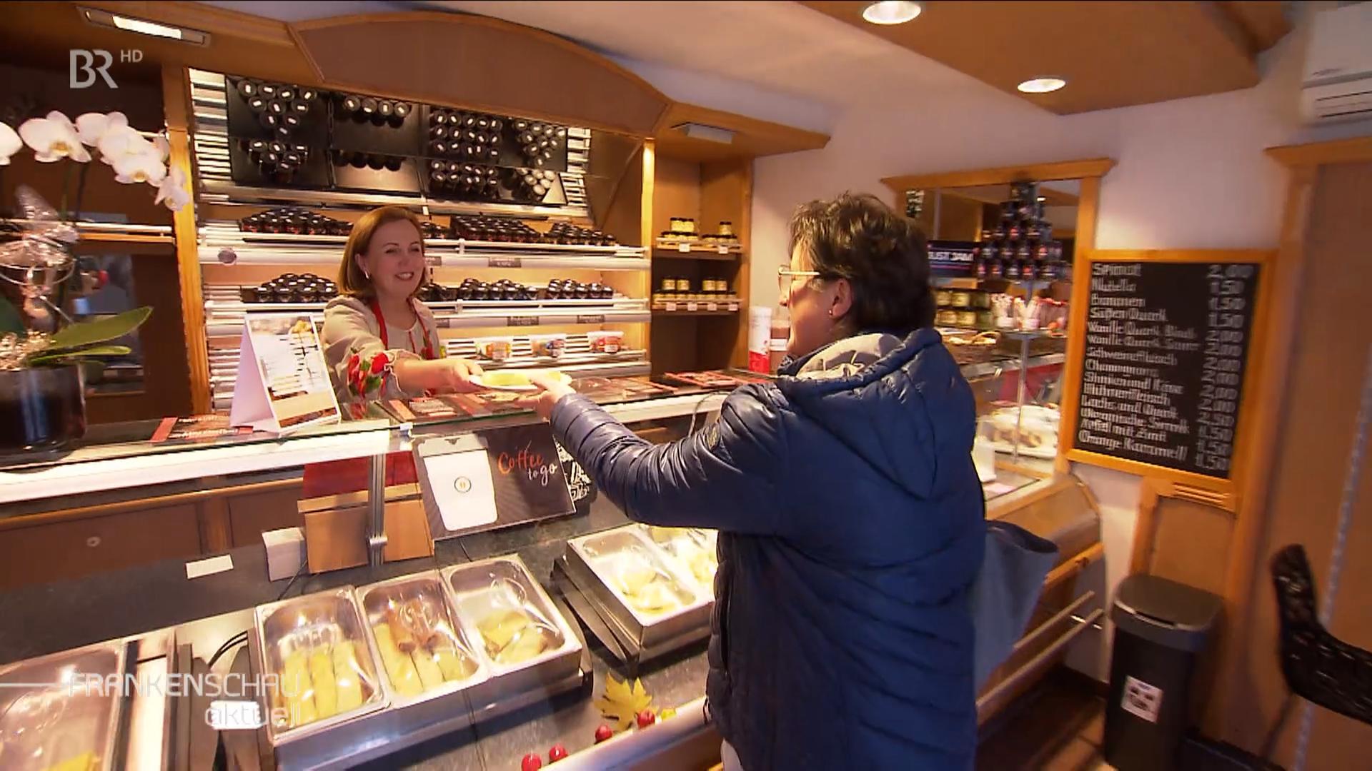 Eine Frau reicht einer Kundin einen Teller mit Pfannkuchen über die Verkaufstheke.