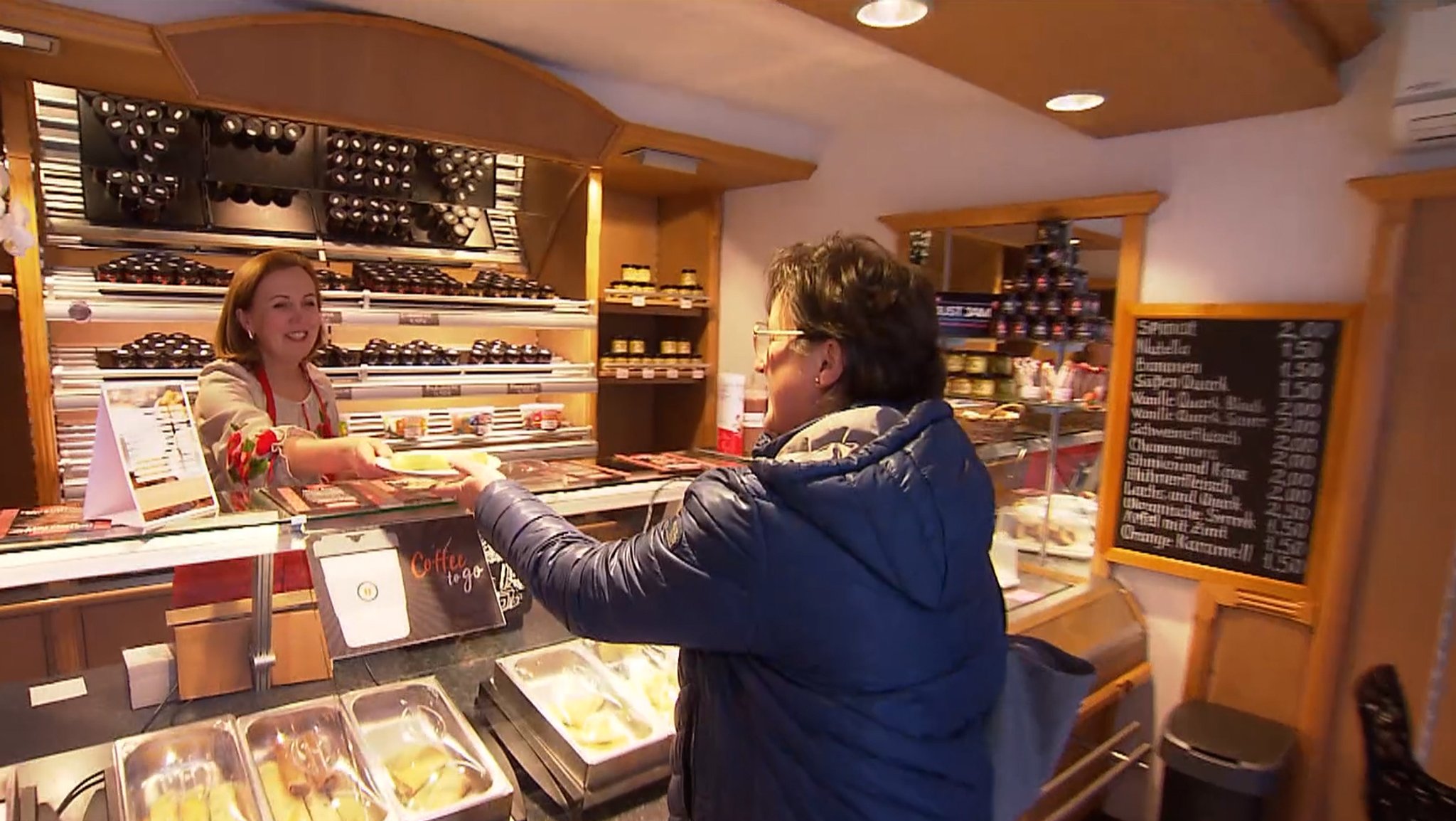 Eine Frau reicht einer Kundin einen Teller mit Pfannkuchen über die Verkaufstheke.