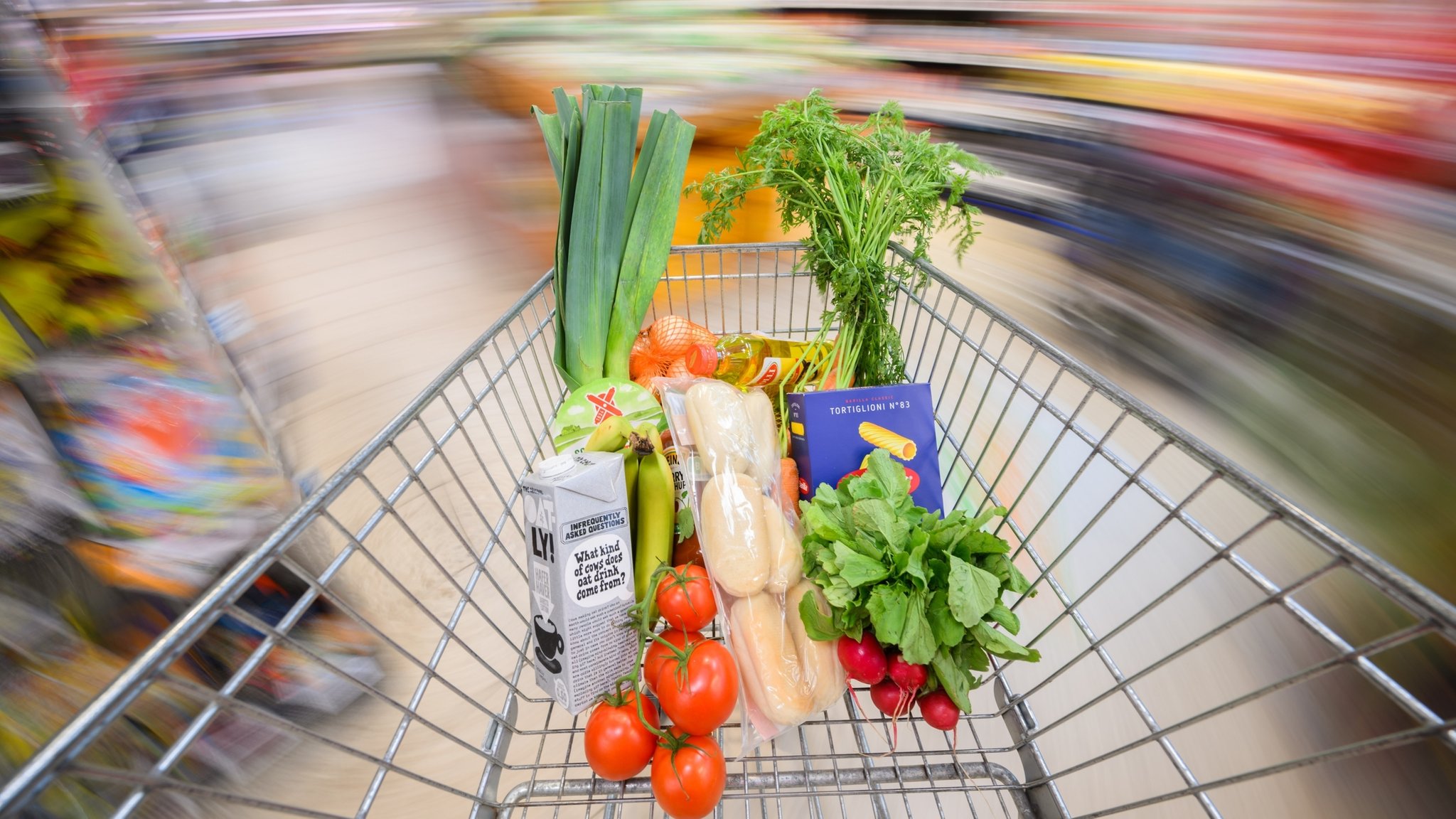 Ein mit Lebensmittel gefüllter Einkaufswagen wird durch einen Supermarkt geschoben
