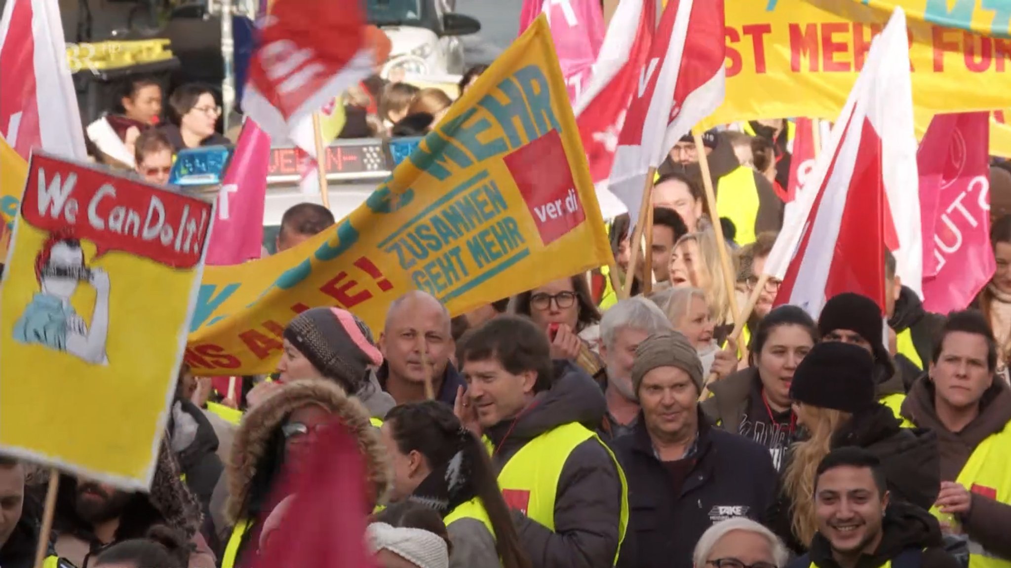 Mehrere Menschen auf Demonstration mit Schildern und Fahnen.