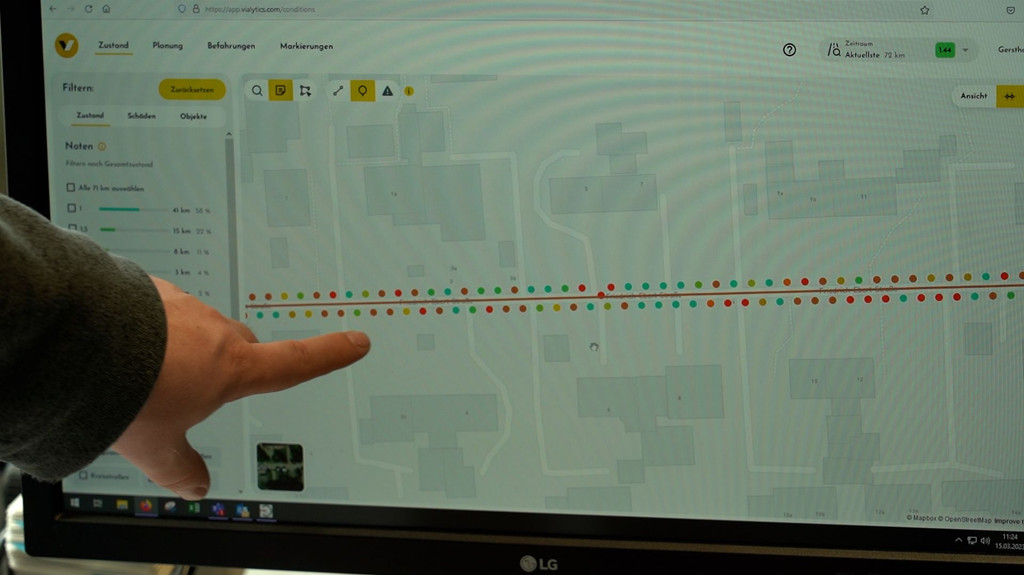 Ein Mann zeigt mit dem Finger auf einen Bildschirm auf dem Punkte in verschiedenen Farben zu sehen sind.