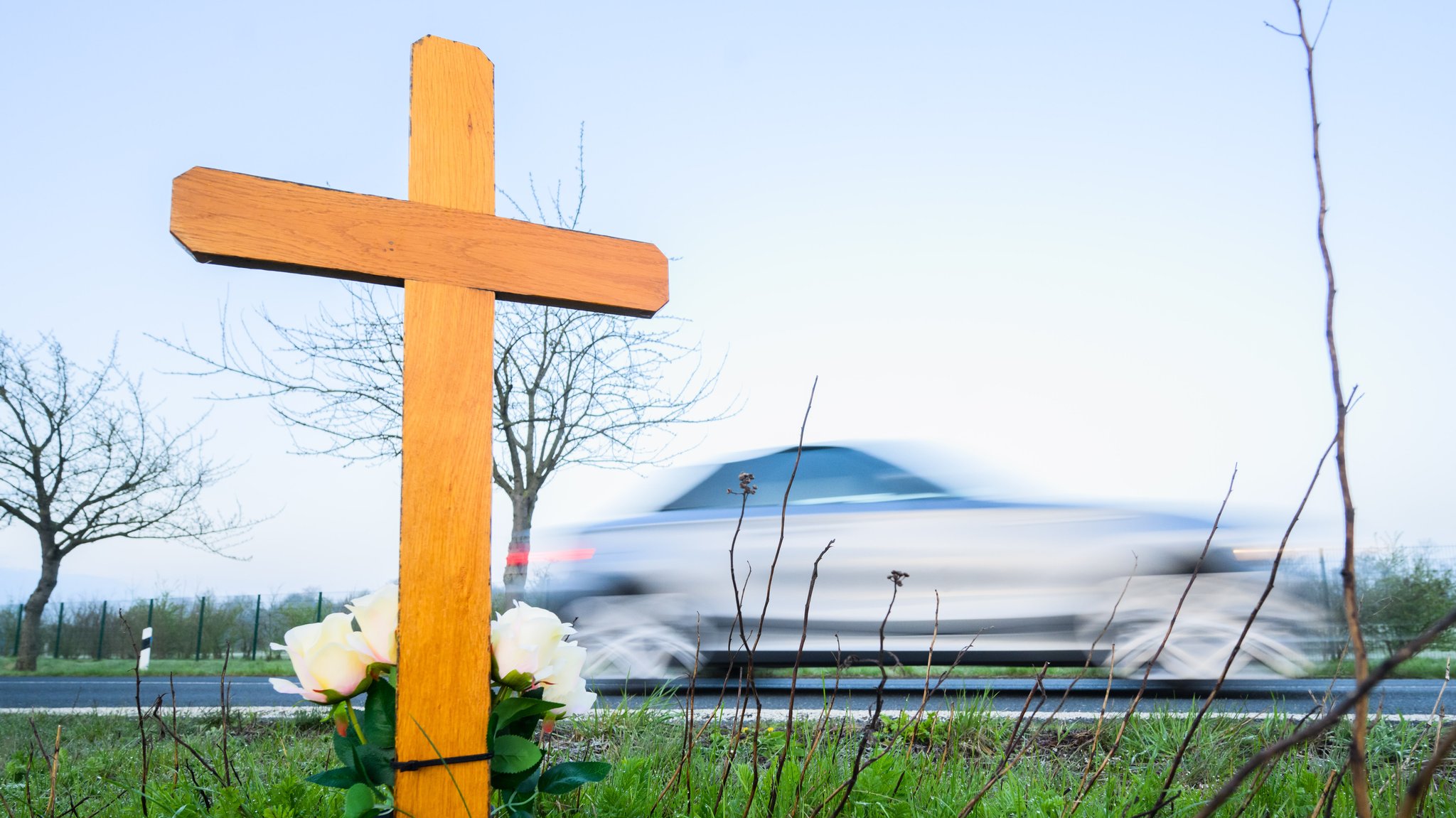 Ein Kreuz zum Gedenken an ein Opfer eines Verkehrsunfalls steht an einer Landstraße.