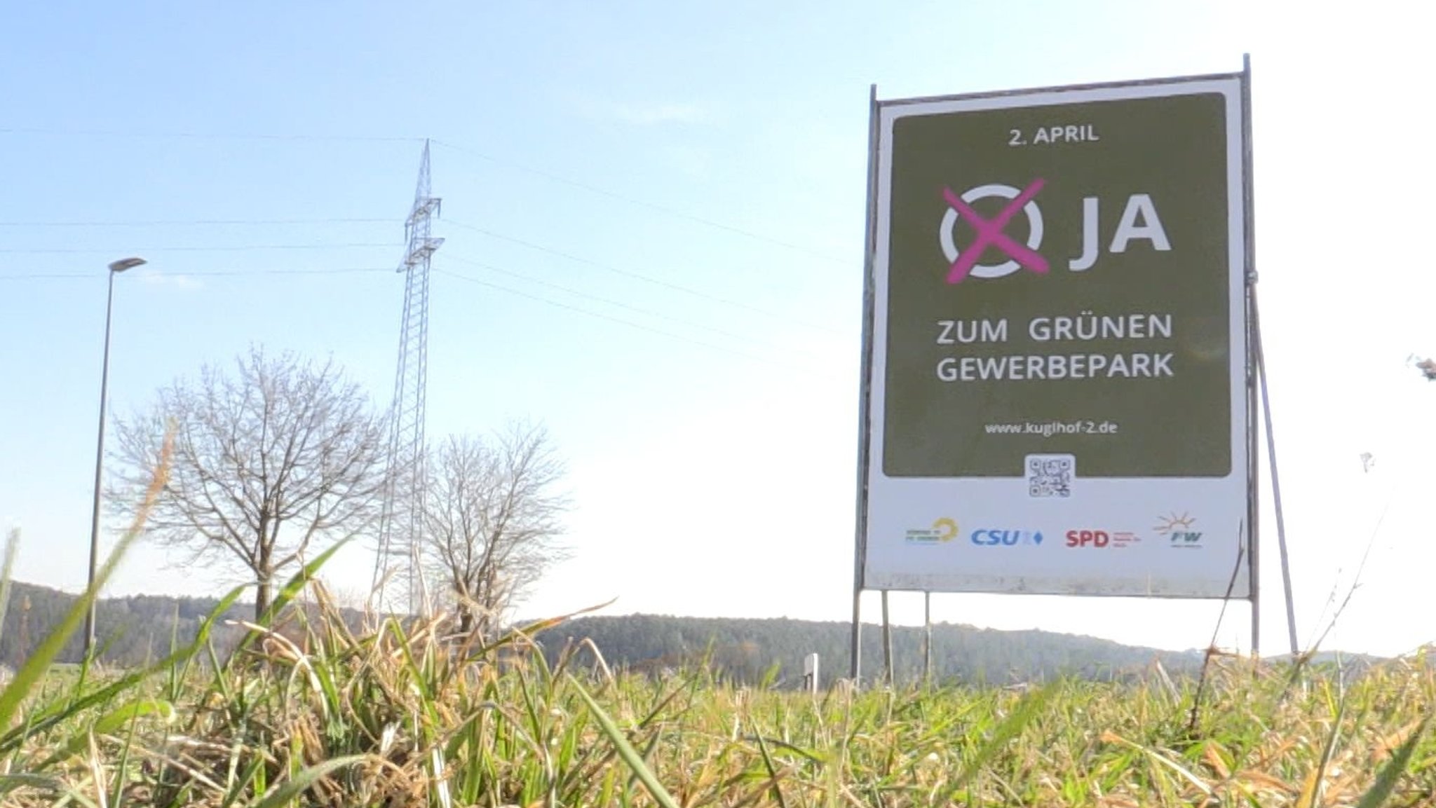 Ein Plakat steht auf einer Wiese. Darauf werben mehrere Parteien für ein "Ja" zum "Grünen Gewerbepark".