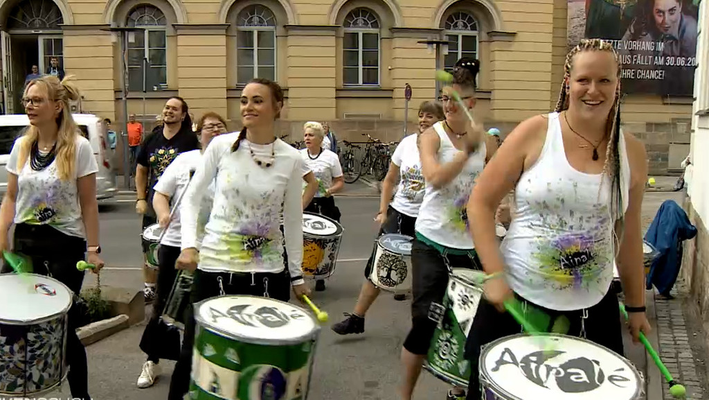 Auf der Straße sind Frauen mit Trommeln unterwegs und machen Musik.